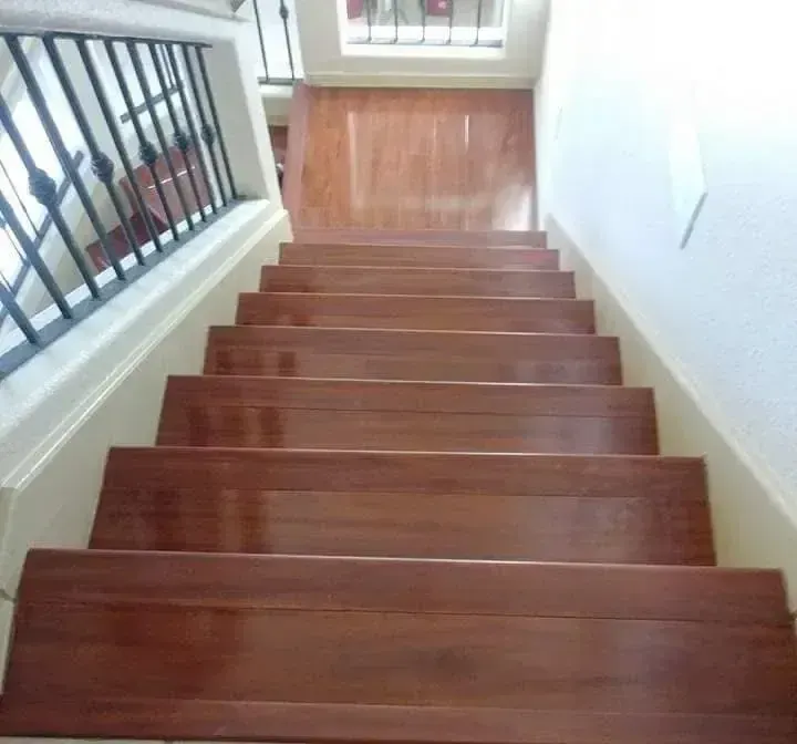Wooden staircase viewed from the top, with a metal railing on the left and white walls.