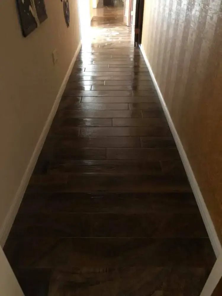 Narrow dim hallway with dark wood floor and beige walls leading to a bright doorway