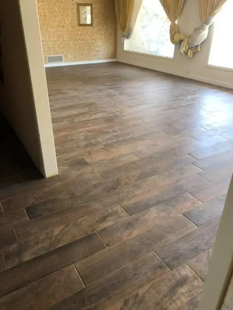 Empty room with dark wood flooring, patterned wallpaper, and large curtained windows.