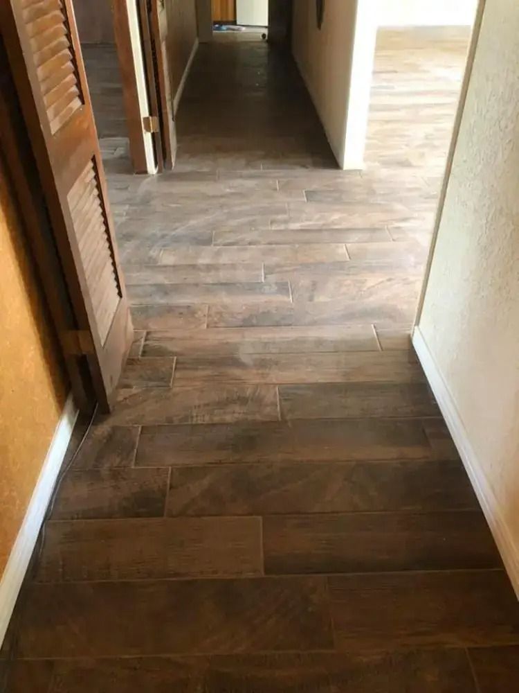 Narrow hallway with dark wood flooring and white walls leading to another room