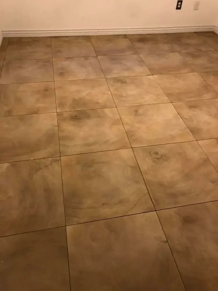 Empty beige tiled room with a white wall and electrical outlet at the back.