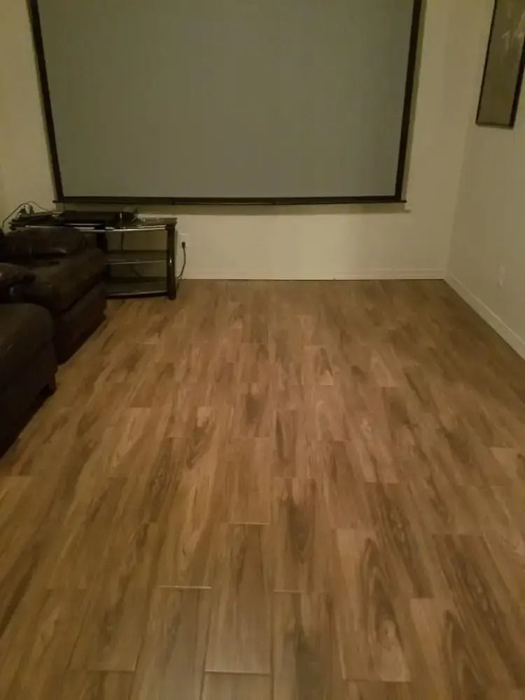 Empty living room with wood flooring, a sofa on the left, and a large projection screen on the wall.