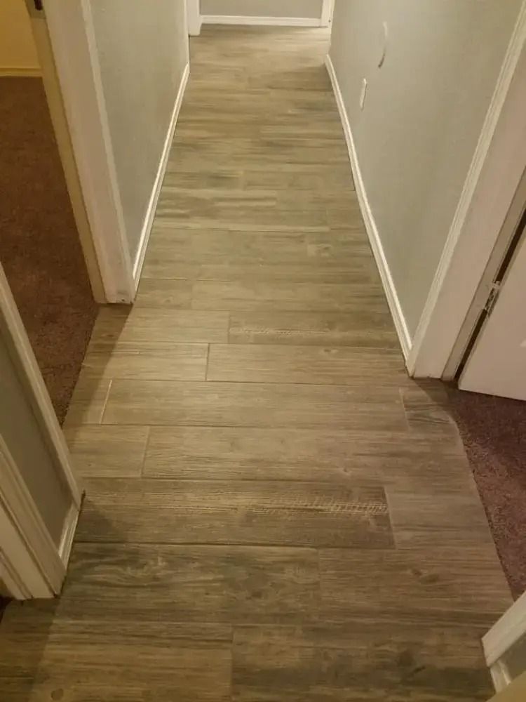 Narrow hallway with light wood flooring and white walls, viewed from one end toward a doorway.