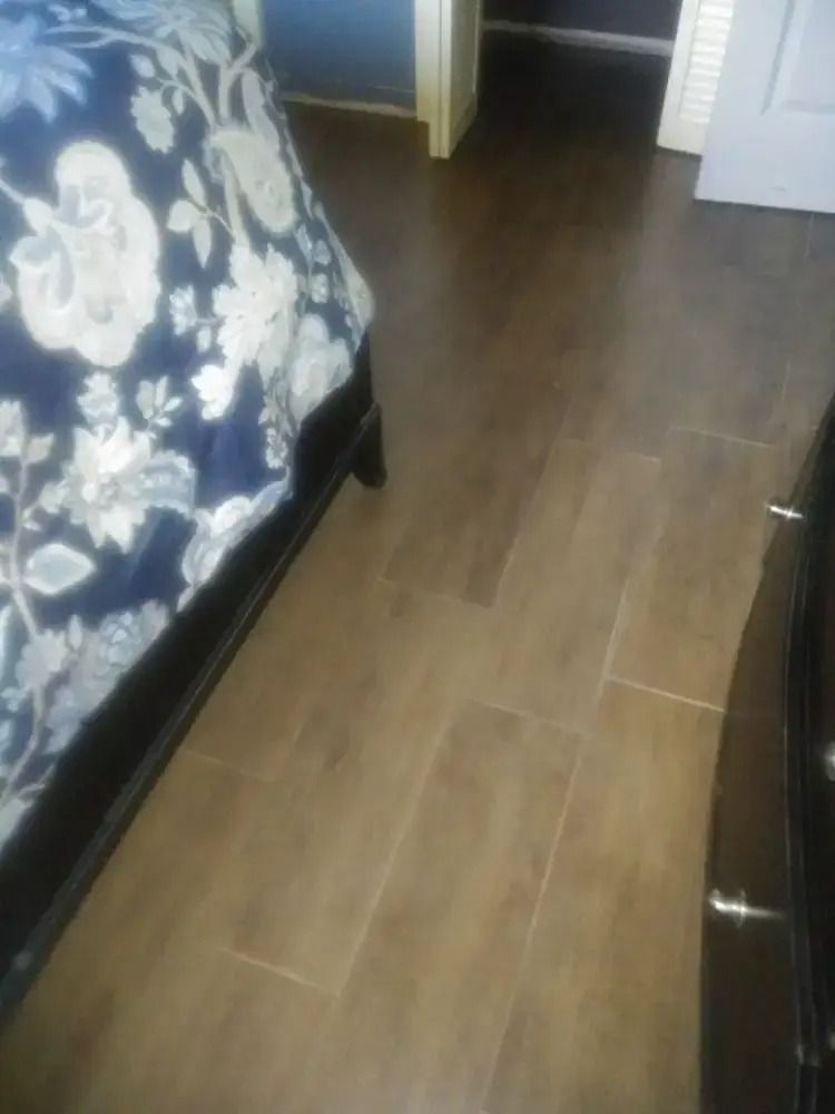 Bedroom floor between a floral bed and a dresser, with brown wood-style flooring.