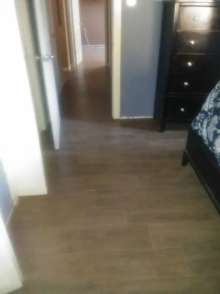 Hallway with wood floor leading to a bedroom and dresser, with a bed partially visible on the right