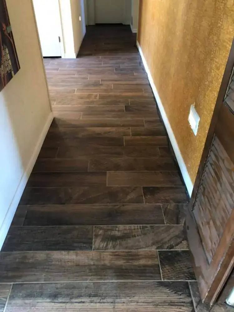 Narrow hallway with dark wood-pattern tile flooring and tan walls leading to a doorway