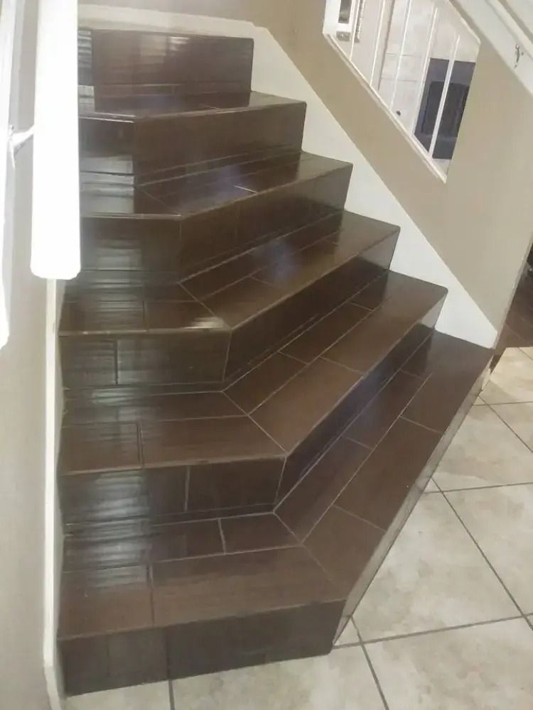 Dark brown tiled staircase with a white handrail and beige floor tiles indoors