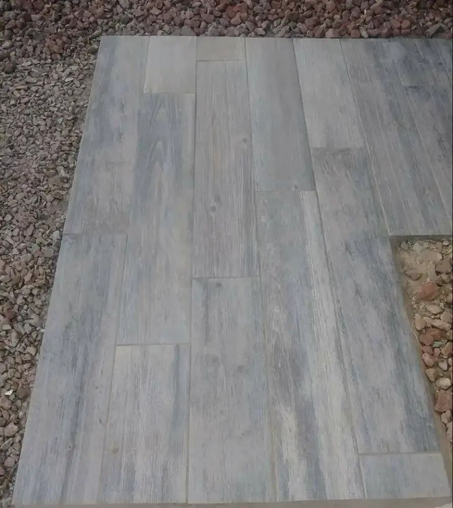 Gray wood-look tile installed on a gravel surface, forming a partial walkway or patio section