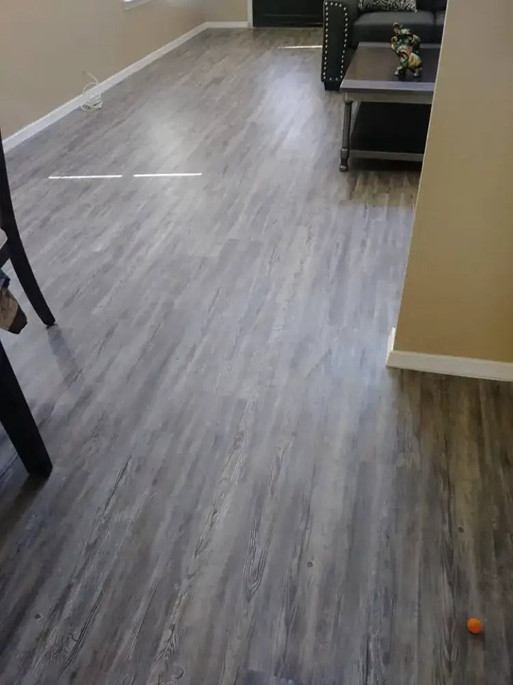 Living room with gray wood floor, beige walls, and a small orange ball on the floor near furniture.