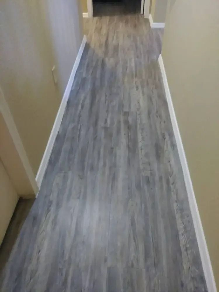 Narrow hallway with gray wood-look flooring and beige walls, viewed from one end toward a doorway.