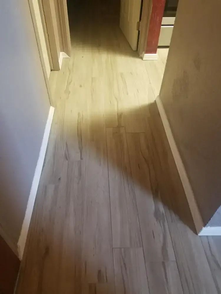 Narrow hallway with light wood floor and white trim, leading to a doorway in the background.