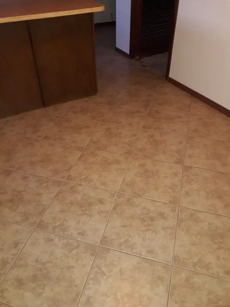 Empty room with tan tile floor, wooden counter on the left, and a doorway in the back.