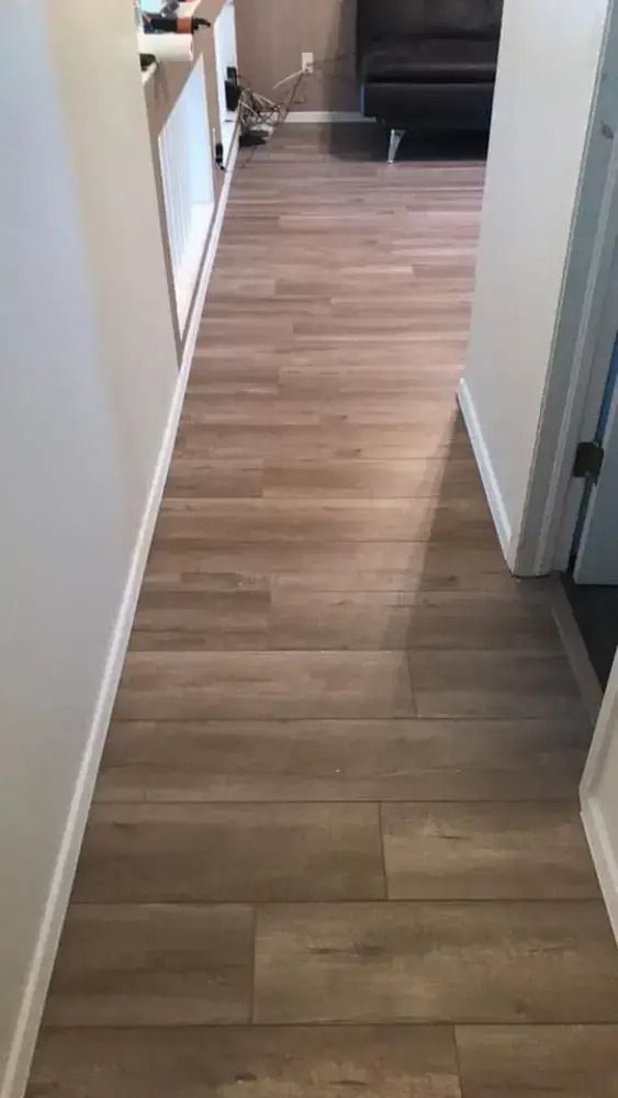 Narrow hallway with light wood flooring leading to a living room and couch at the end.