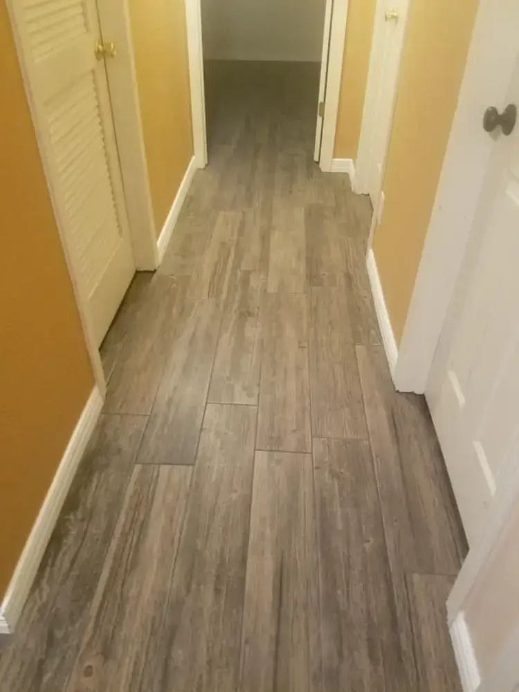 Narrow hallway with gray wood-look tile flooring and white doors on yellow walls.