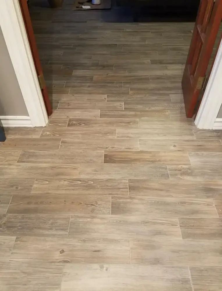 Wood-look tile floor in a hallway doorway, with beige walls and a wooden door on the right.