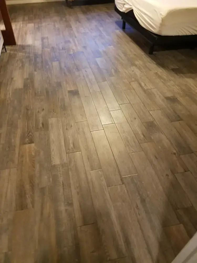 Wooden floor in a bedroom with a bed visible at the right edge.