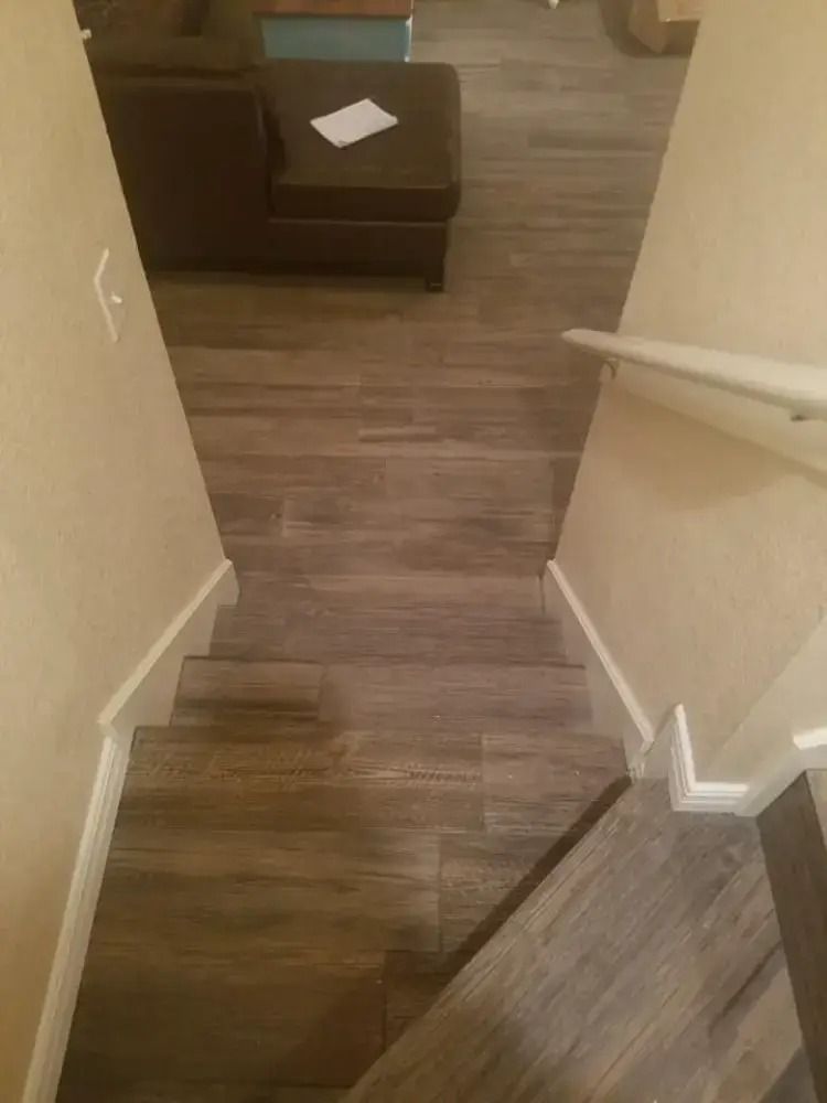 Stairway with wood flooring leading down to a small living area with a dark ottoman and a handrail on the right