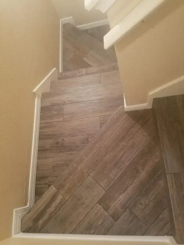 Narrow indoor staircase with wood-pattern flooring and beige walls, viewed from the top down