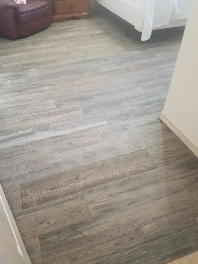 Gray wood-look floor in a bedroom doorway, with a bed and chair partially visible.