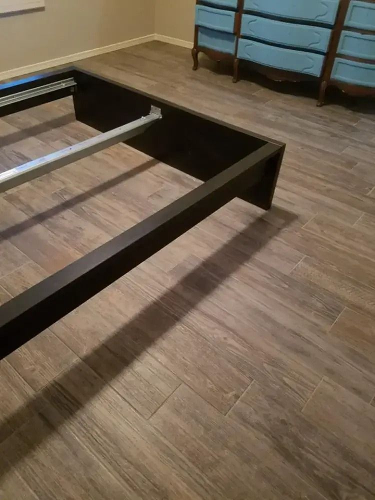 Partially assembled dark wood bed frame on a wood floor in a bedroom