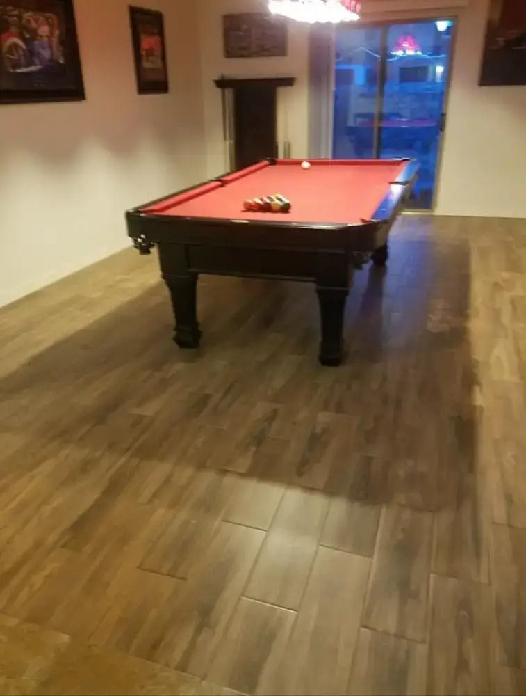 Pool table in a room with wood floors and a window, viewed from the corner.
