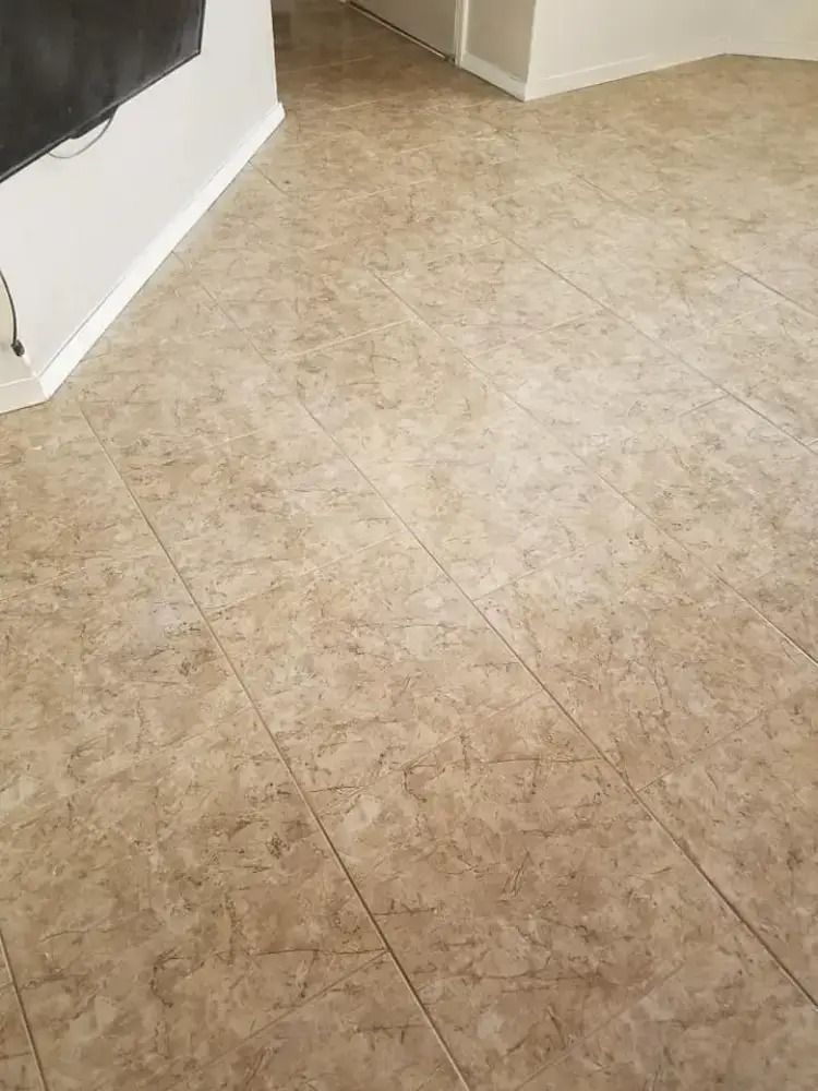 Empty room with beige tile floor and white baseboards, viewed from a corner