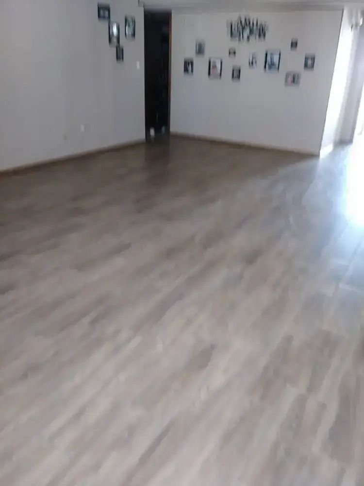 Empty room with light wood flooring, white walls, and framed photos on the far wall.