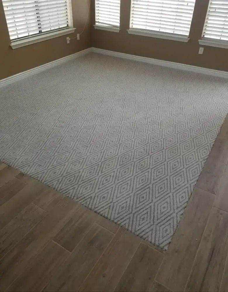 Empty room with light patterned carpet and hardwood floor near windows with blinds