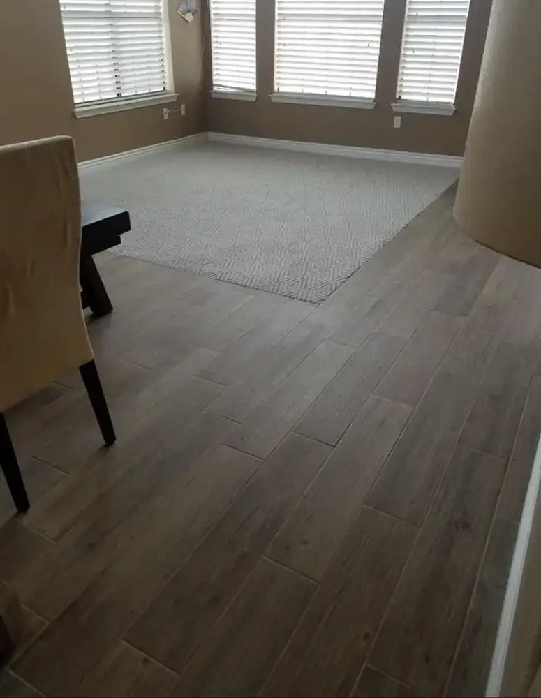 Empty room with light wood flooring, a beige rug, and windows with blinds letting in daylight