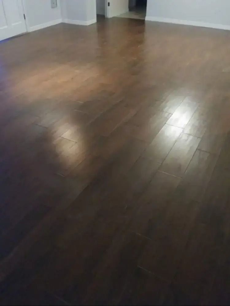 Empty room with dark hardwood floors and white walls, lit by natural light.