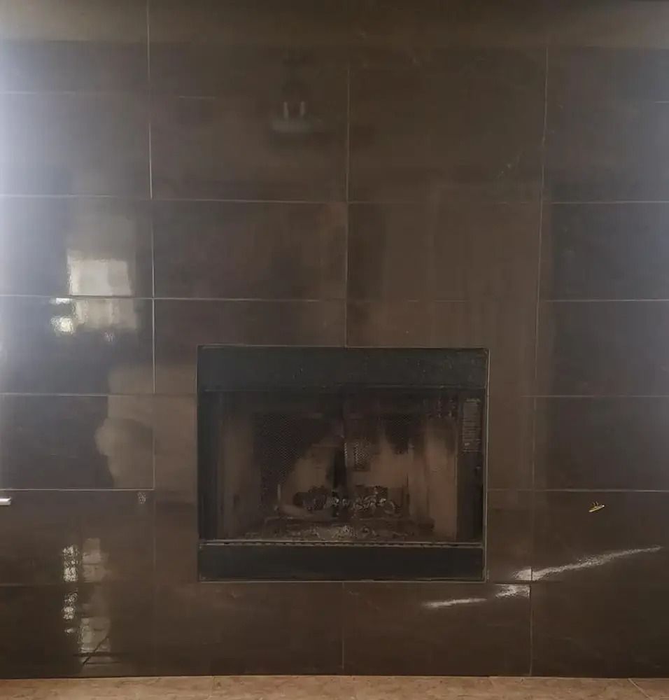 Dark tiled fireplace with a glass front and faint reflection in a dim room