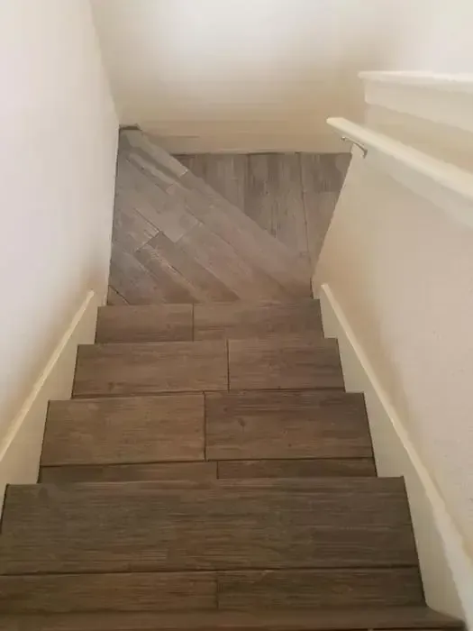 Narrow indoor staircase with dark wood steps descending to a lower landing and white walls.