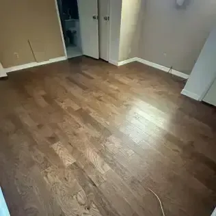 Empty room with brown wood floors, beige walls, and a small open closet doorway