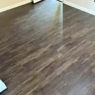 Empty room with dark wood laminate flooring and beige walls, viewed from a corner.