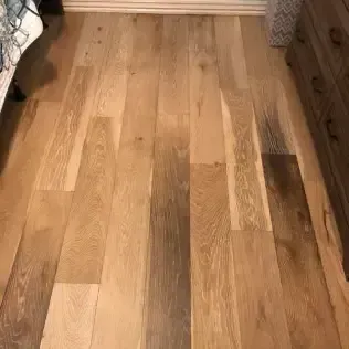 Wooden floorboards in a narrow room between a bed and a dresser.