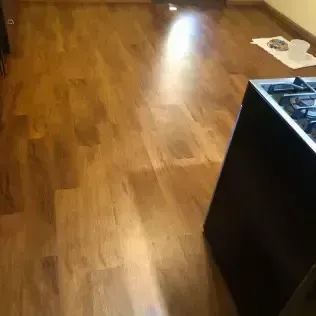 Empty wood-floored room with a dark kitchen island and a small white paper on the floor.