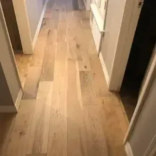 Narrow hallway with light wood flooring and white doorframes leading to a brighter room.