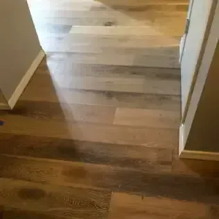 Wooden floor hallway leading to a brighter room, with beige walls and white trim.