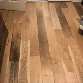 Wooden plank floor in a kitchen or hallway, with cabinets at the top edge and a shoe visible on the right.