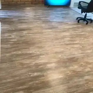 Wood-look office floor with a brick wall, glowing screen in back, and a rolling chair at right.