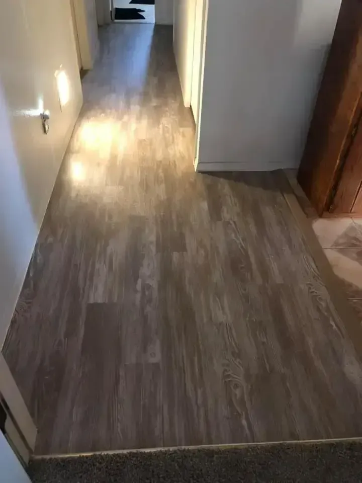 Empty hallway with wood-look flooring and soft wall lighting leading to a doorway.