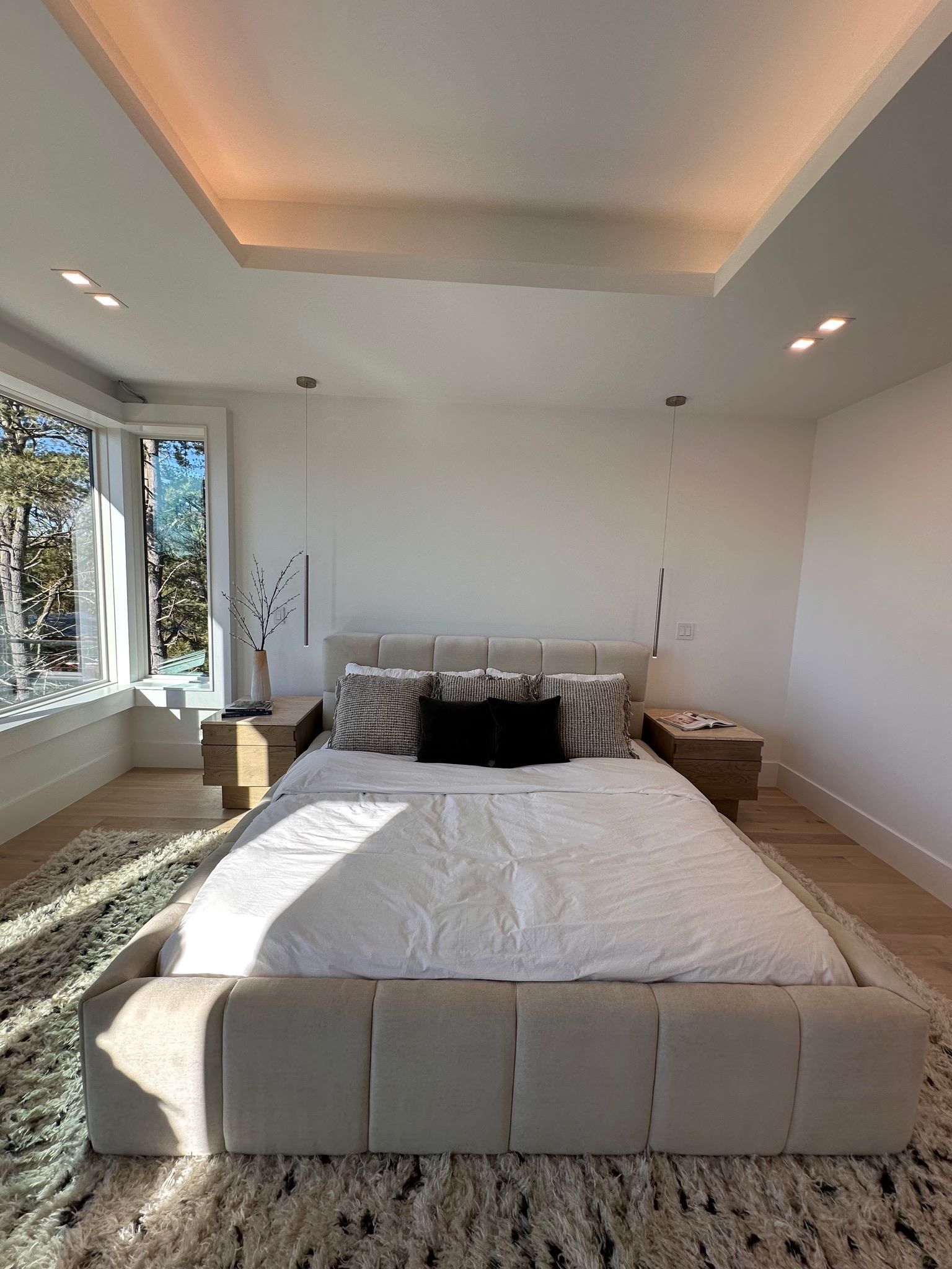 Bright bedroom with a low white bed, large windows, and warm recessed ceiling lighting