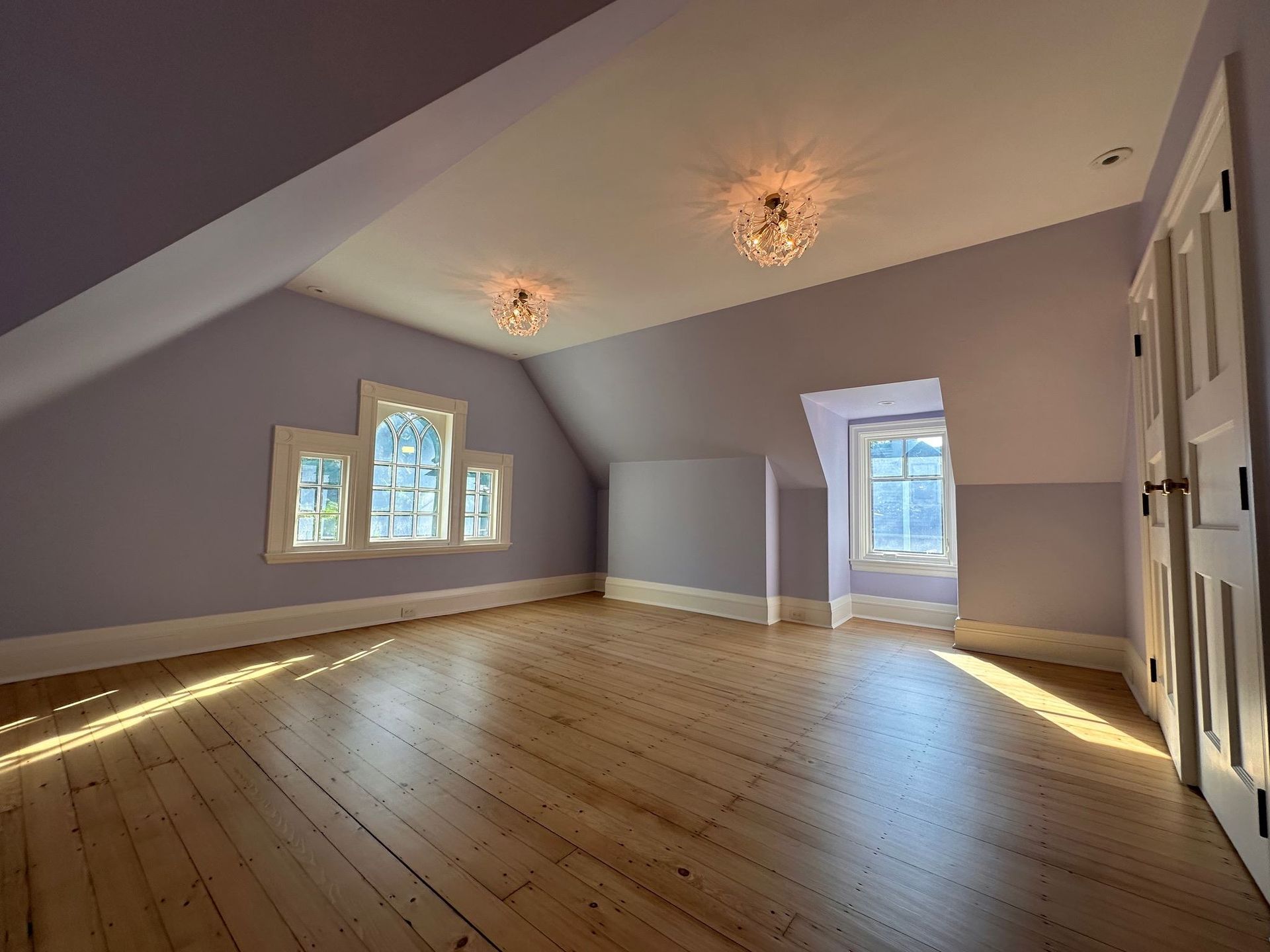 Empty attic-style room with sloped gray walls, wooden floor, and several windows letting in daylight