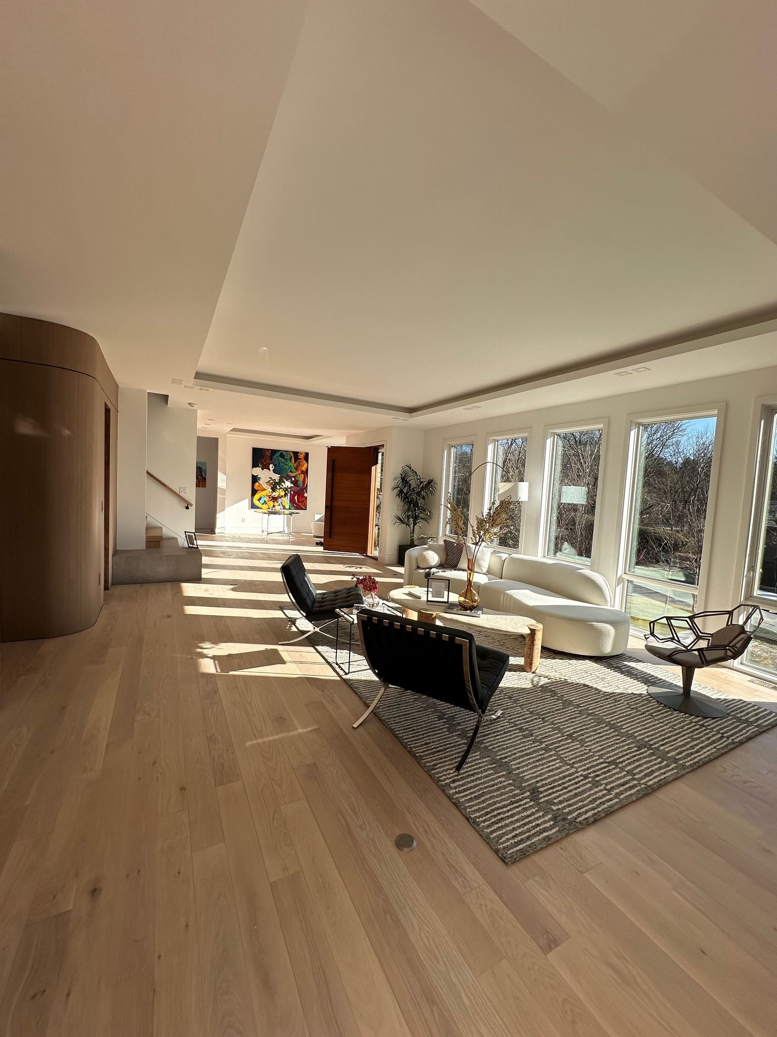 Modern living room with large windows, wood floors, white walls, and black lounge chairs in bright sunlight