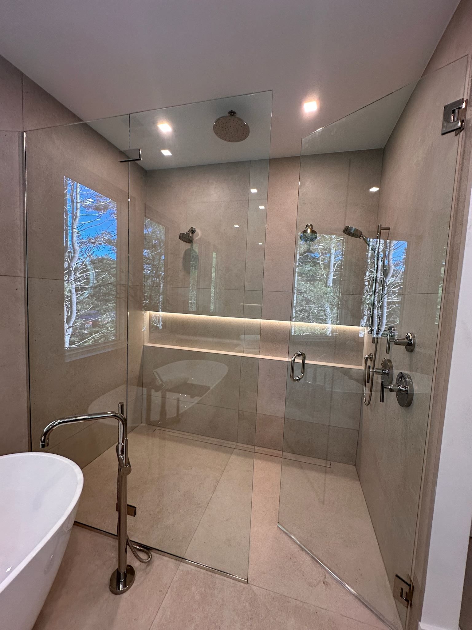 Modern glass shower bathroom with beige tile, handheld shower, and vanity mirror wall