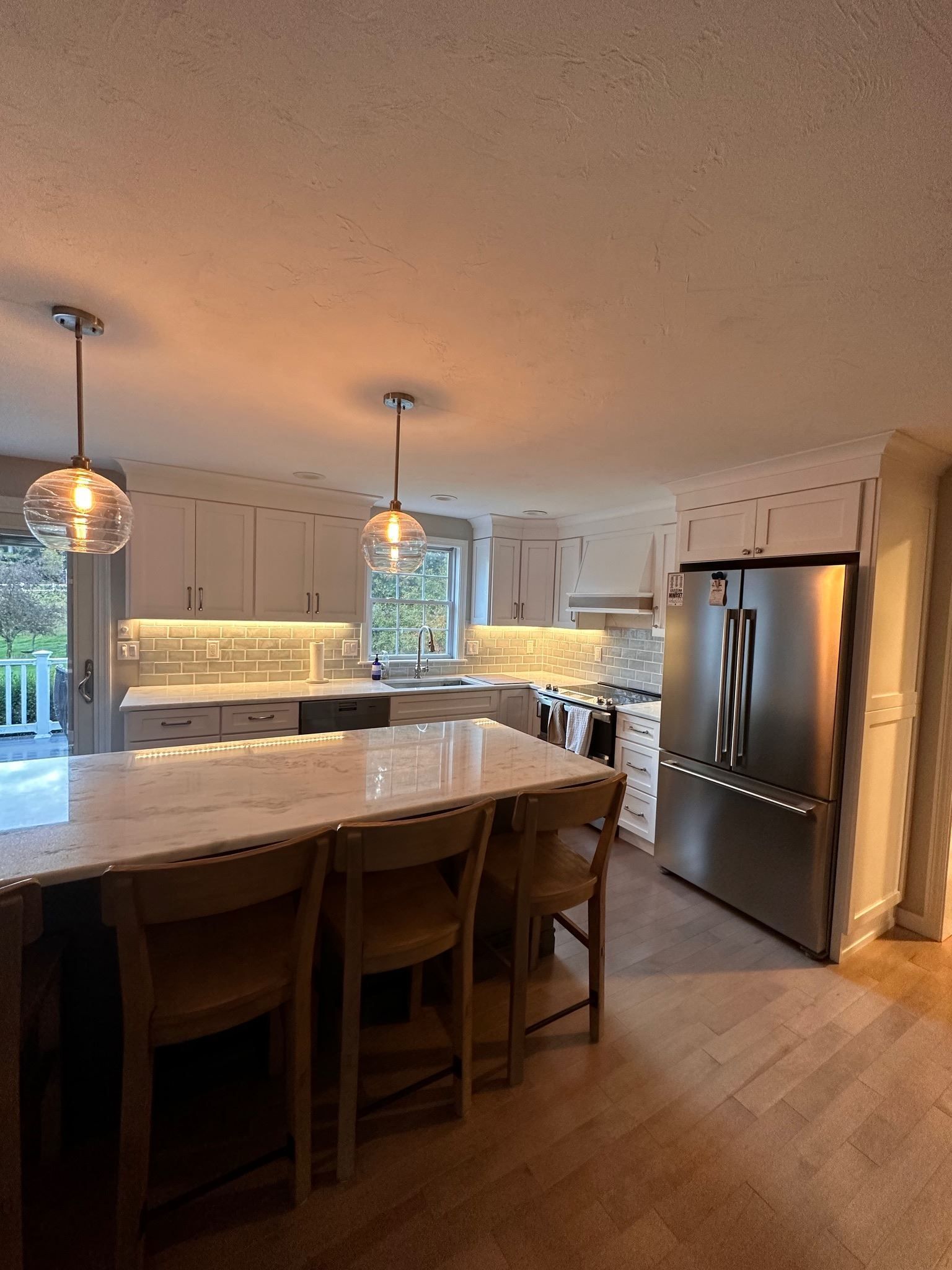 Modern kitchen with island, pendant lights, stainless steel fridge, and wood floors