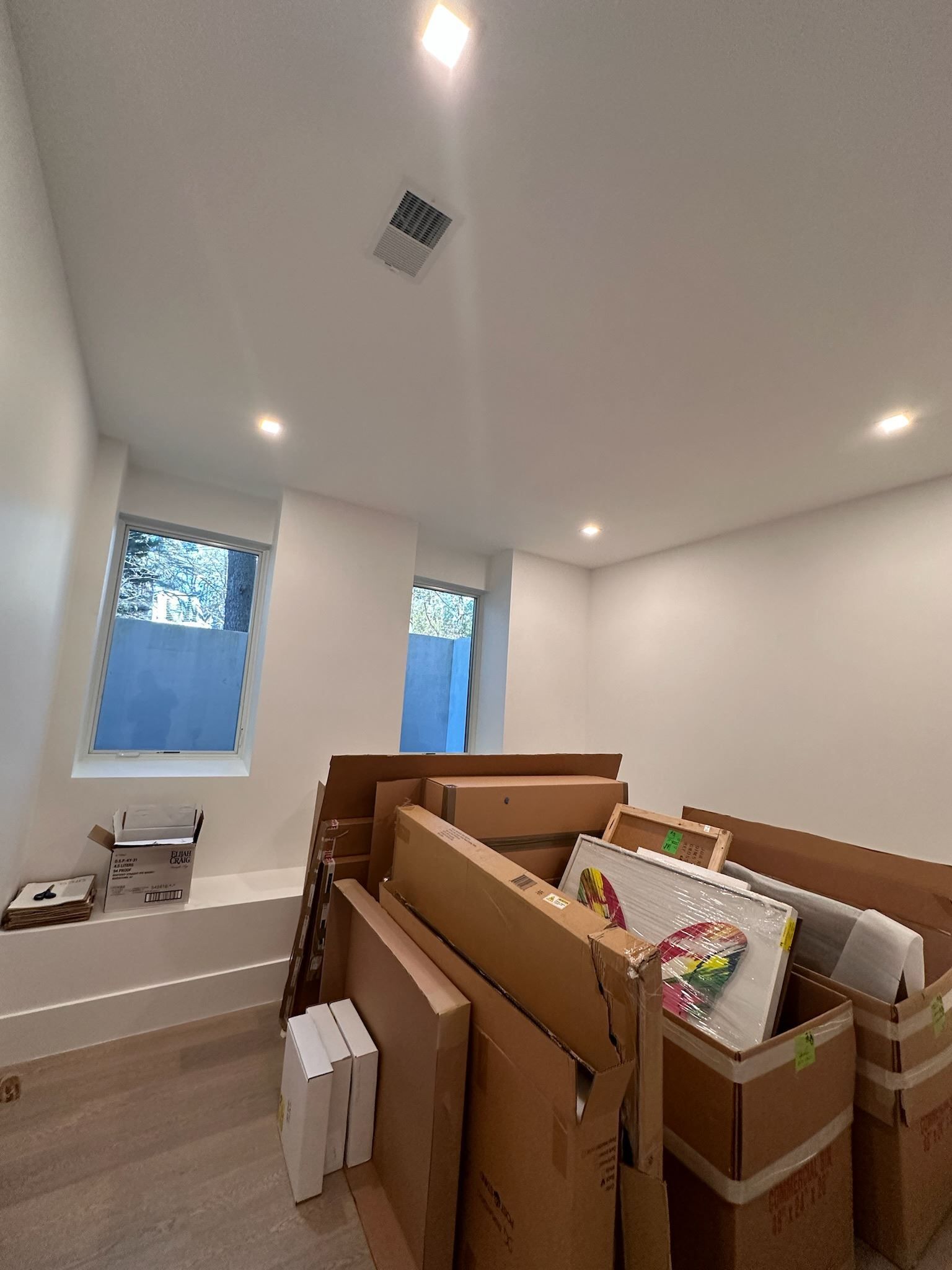 Unfinished room with stacked boxes, white walls, recessed lights, and windows by a bathtub alcove