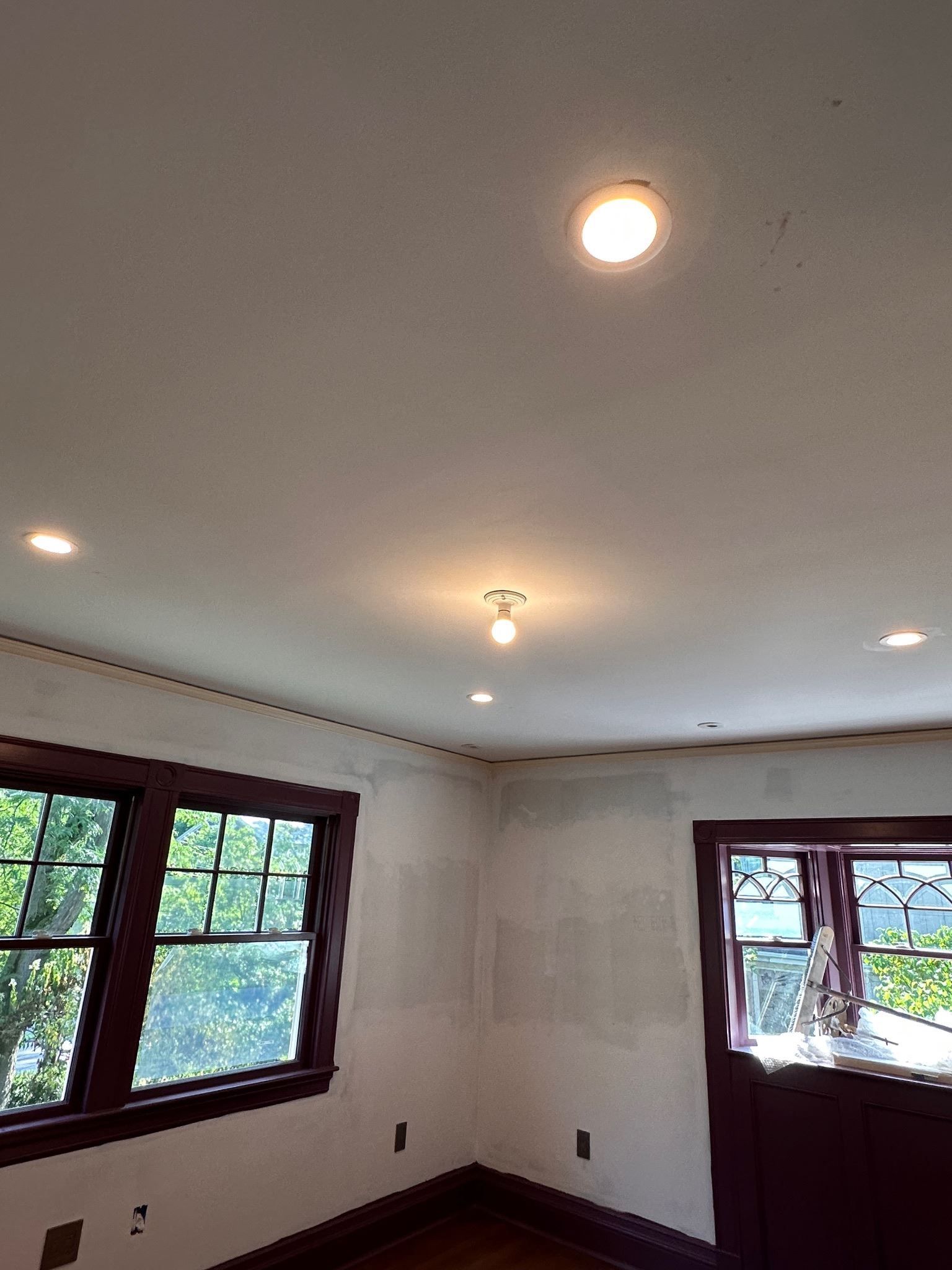 Empty white room with recessed lights, wood-trimmed windows, and a view outside.