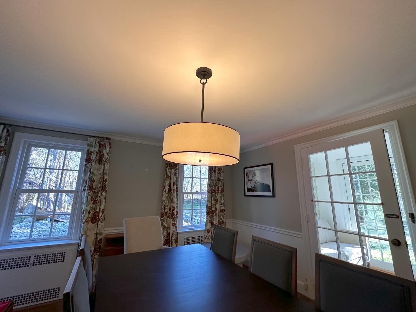 Dining room with a round table, beige pendant light, windows, and glass doors leading outside.