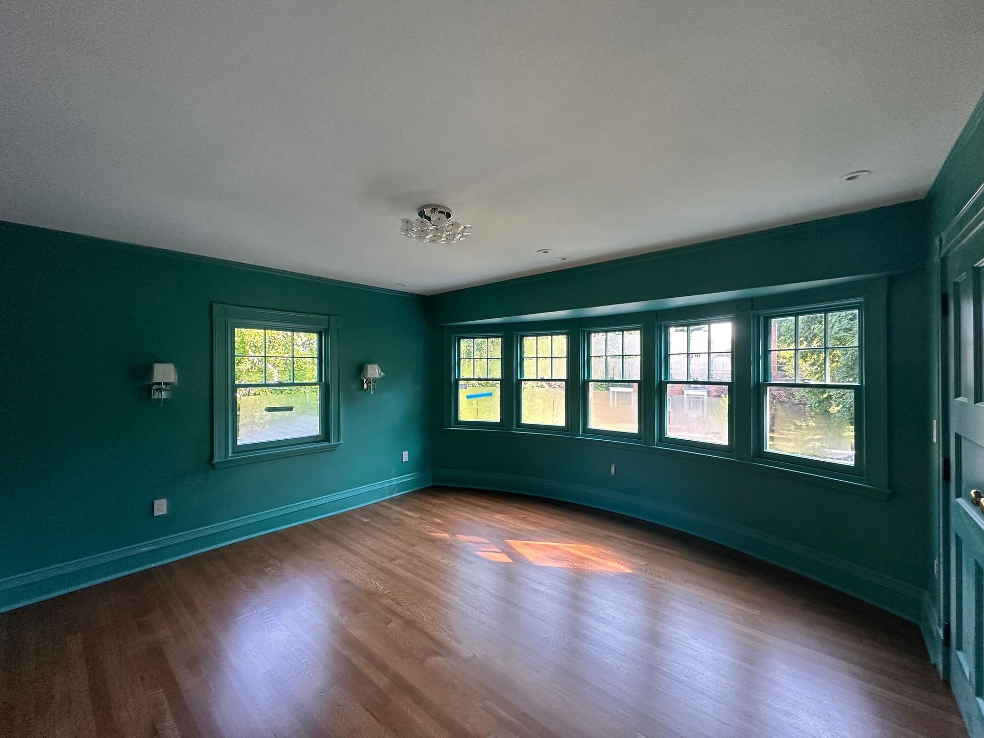 Empty teal living room with hardwood floors and large windows letting in natural light